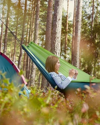 Zwei junge Frauen in einer Hängematte beim Zelten im Wald. 